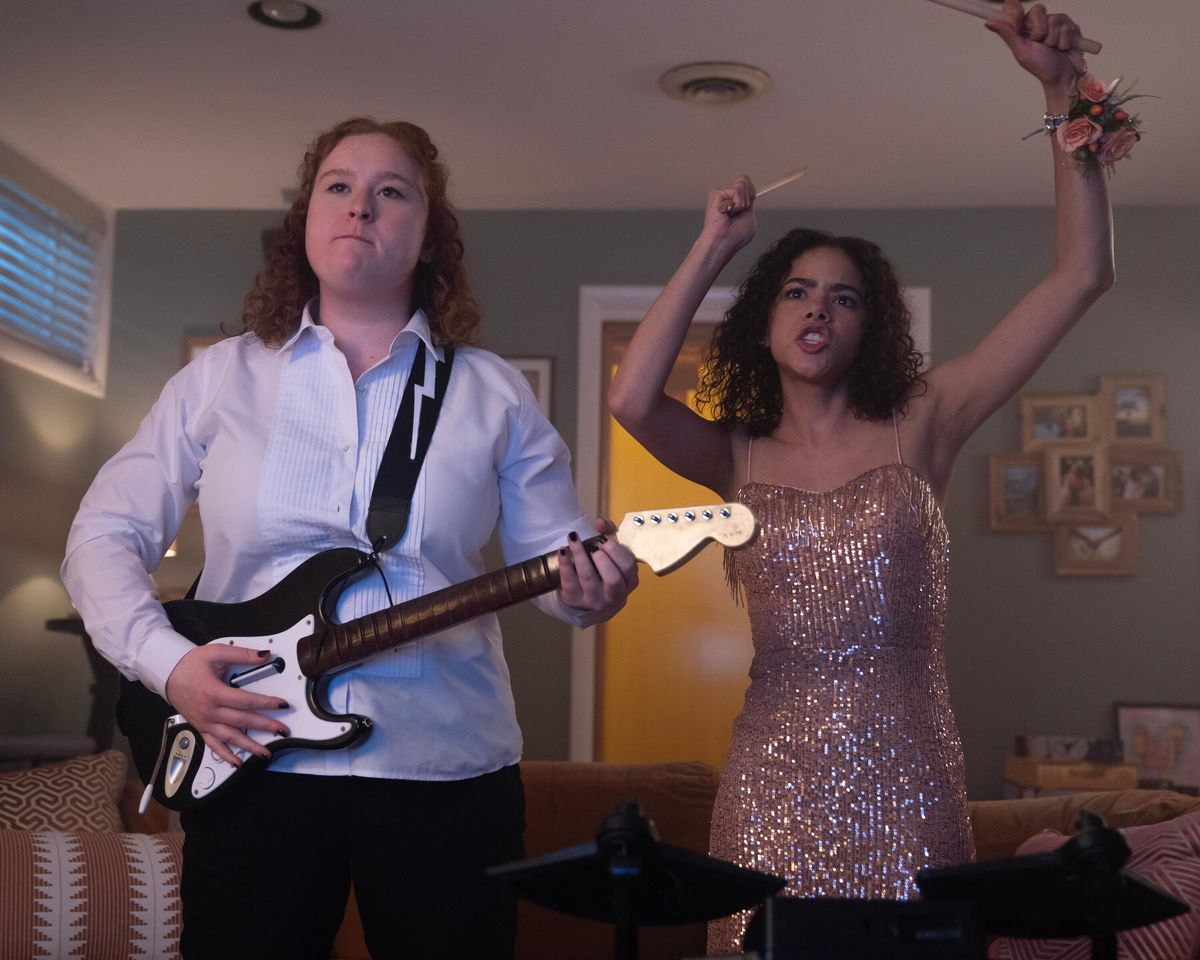 Two girls in prom attire playing with a plastic guitar and drum sticks in Prom Dates.
