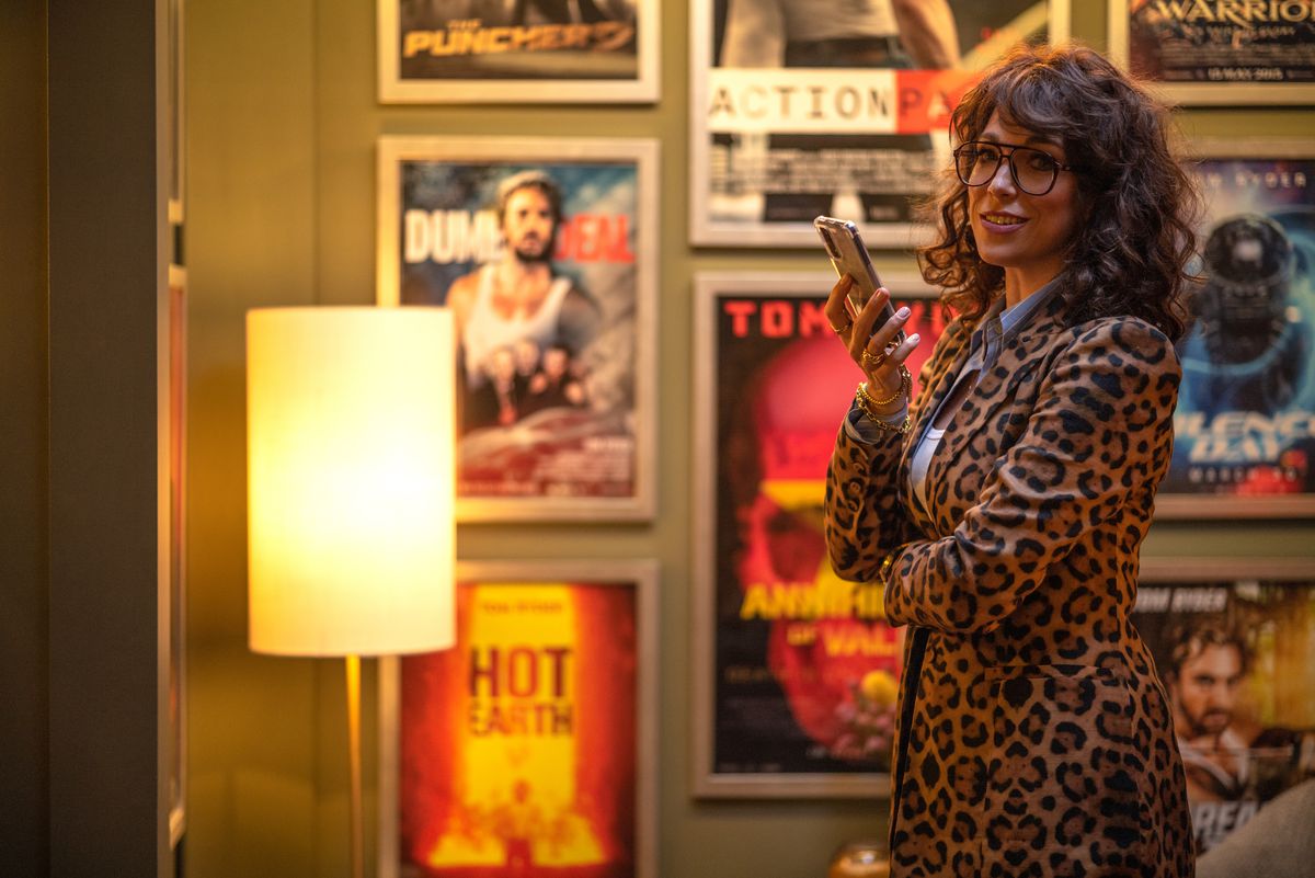 In a scene from The Fall Guy, producer Gail Meyer (Hannah Waddingham, in a leopard-print wrap dress) stands in a room lined with movie posters, holding up her phone
