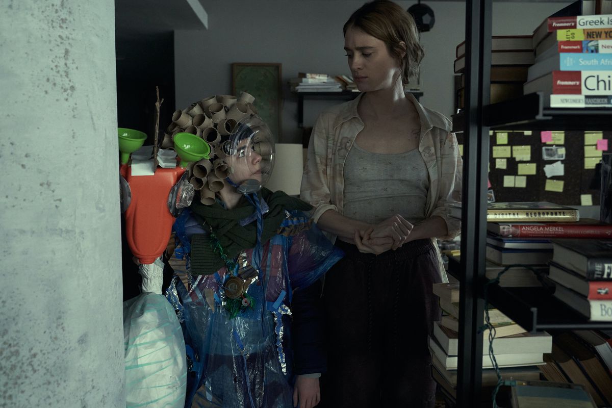 Older Kirsten (Mackenzie Davis) looks down at Younger Kirsten (Matilda Lawler) in a crowded apartment