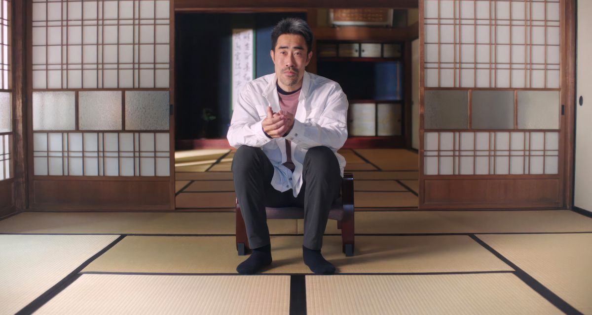 The Contestant subject Nasubi in a modern-day interview, sitting on a tatami-floored room in front of open shoji, with his hair neatly cut short