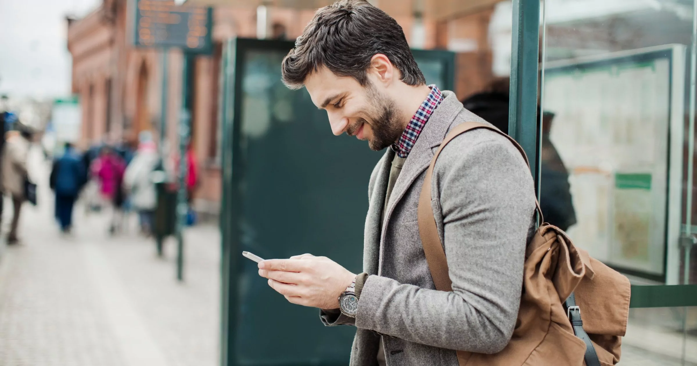 Man smiling at iphone in his hand while on sidewalk