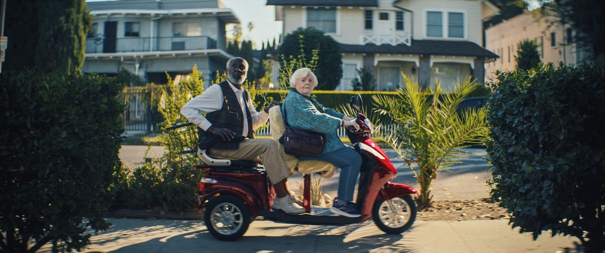 June Squibb and Richard Round Tree as Thelma and Ben, look to their right as they motor down the sidewalk on a two-seater mobility scooter in Thelma.