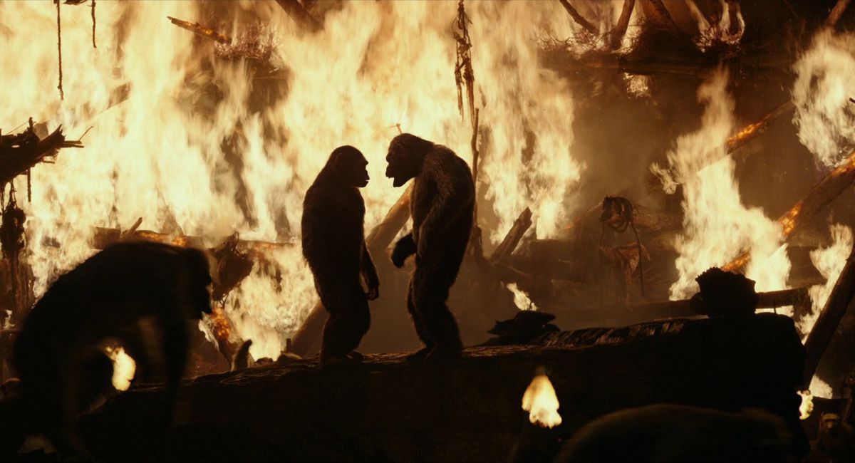 Two apes facing one another atop a platform surrounded by apes fleeing a burning structure.