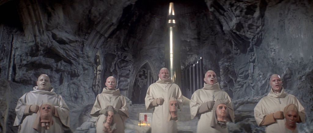 A group of bald figures dressed in monk garbs and holding mannequin heads in a cavern with a large church-like interior in Beneath the Planet of the Apes.