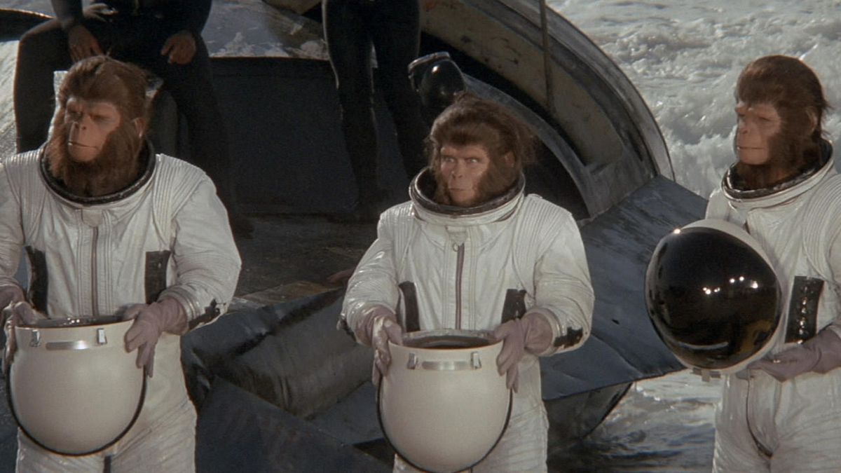 Three apes in astronaut suit standing side by side holding helmets in Escape from the Planet of the Apes.